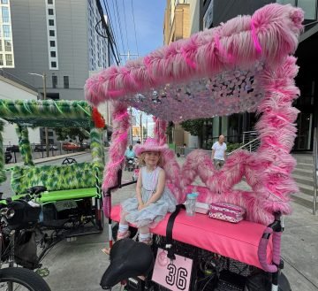 A pink furry Local Bike Taxi with a three-year-old in a pink cowboy hat riding on the front seat. 