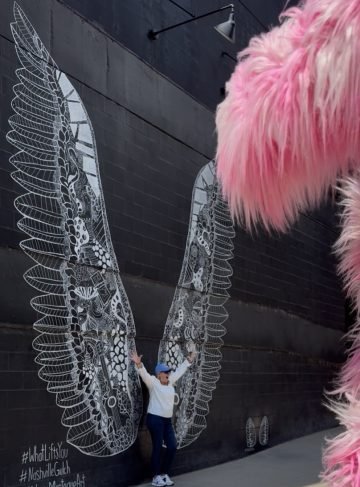 A grandma taking a picture in front of the Nashville Whatliftsyou wing mural in the Gulch. 