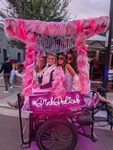 Four ladies riding in a pink pedicab to a football game. 