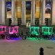 A picture of pink and green furry 6 seating bill board pedicabs in Nashville, in front of some CMA fest banners.