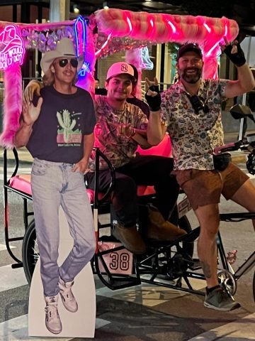 Guys riding on a furry pink pedicab in Nashville, Tennessee, carrying a life-sized poster of Alan Jackson.