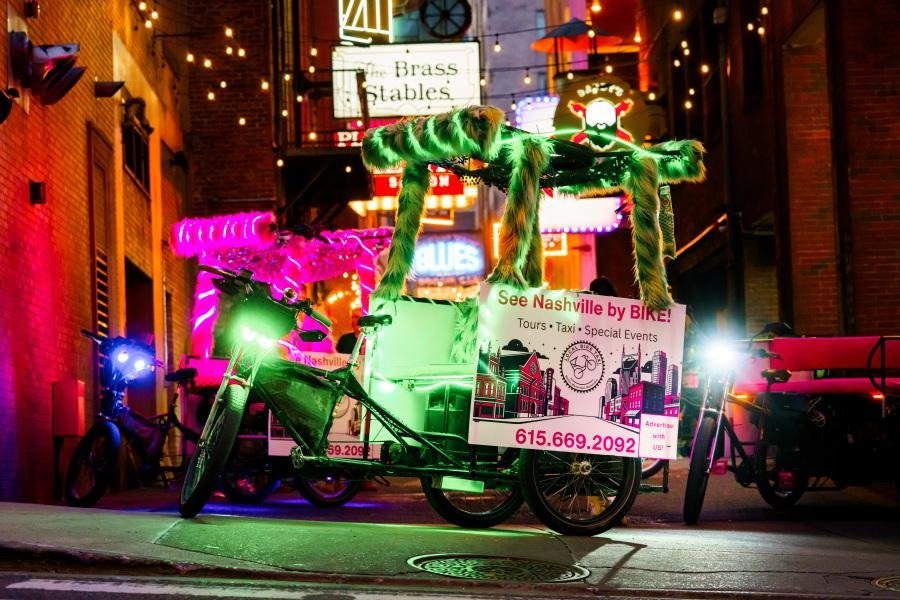 Pink and Green neon pedicabs in Printers Alley. These pedicabs have large canopies on them that are accented with fur. 