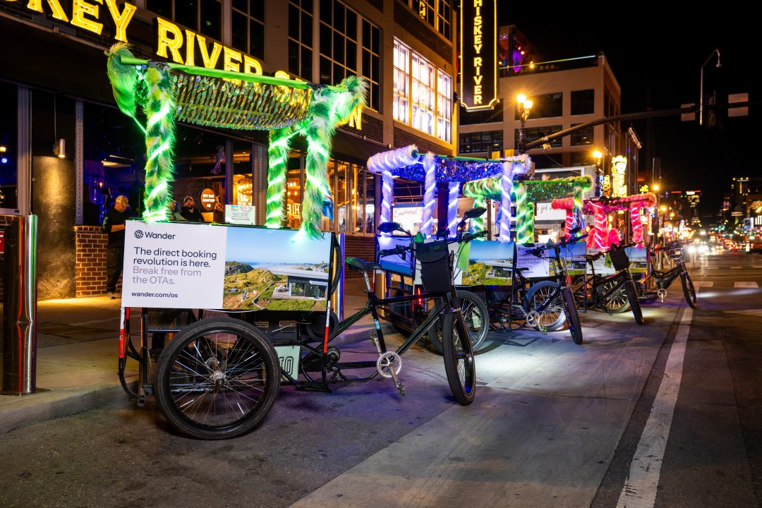 Neon lit Pedicabs with Wander Ad campaign on them parked on Broadway in Nashville. Lots of bright lights and tourist in cowboy hats.