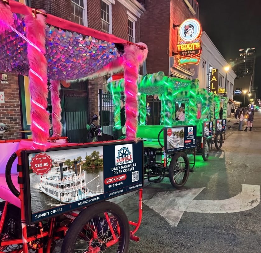 Pink and Green Neon and furry pedicabs on Rep John Lewis Blvd in Nashville Tennessee with ads on them for the river boat.