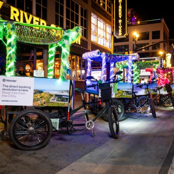 Neon lit Pedicabs with Wander Ad campaign on them parked on Broadway in Nashville. Lots of bright lights and tourist in cowboy hats.